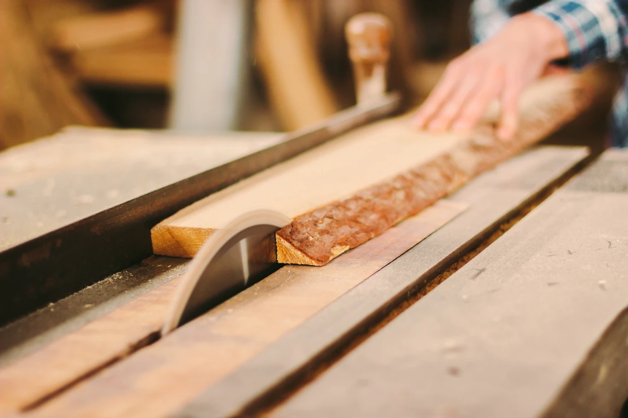 Atelier de menuiserie avec artisan travaillant le bois, planches de bois brut disposées sur établi