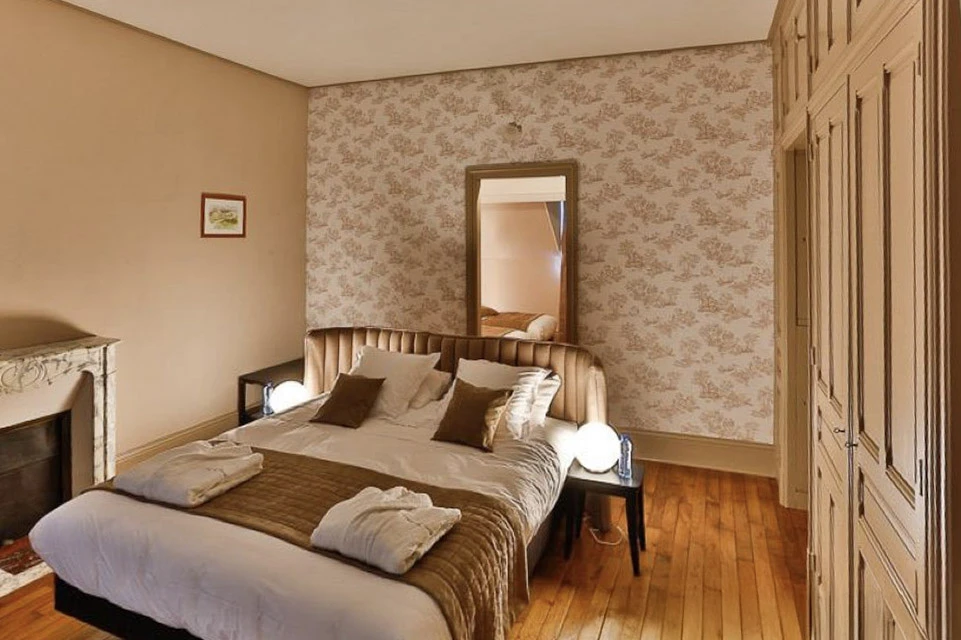 Chambre d'hôtel élégante avec lit double, tête de lit en bois sculpté, papier peint floral beige sur mur d'accent