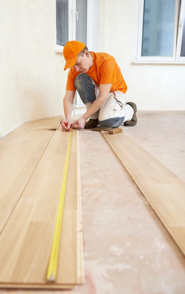 Ouvrier installant du parquet en bois clair dans un intérieur résidentiel, main positionnée sur une lame pour ajustement précis