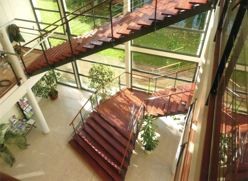 Escalier en colimaçon vue plongeante depuis étage supérieur, rampe bois courbée avec barreaux métalliques noirs, marches bois massif, sol carrelage damier noir et blanc au rez-de-chaussée