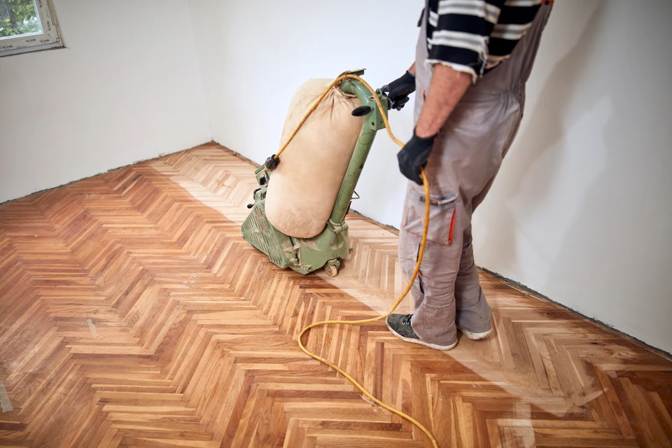 Une personne portant des gants blancs applique un produit de réparation sur du parquet en bois avec un outil de précision